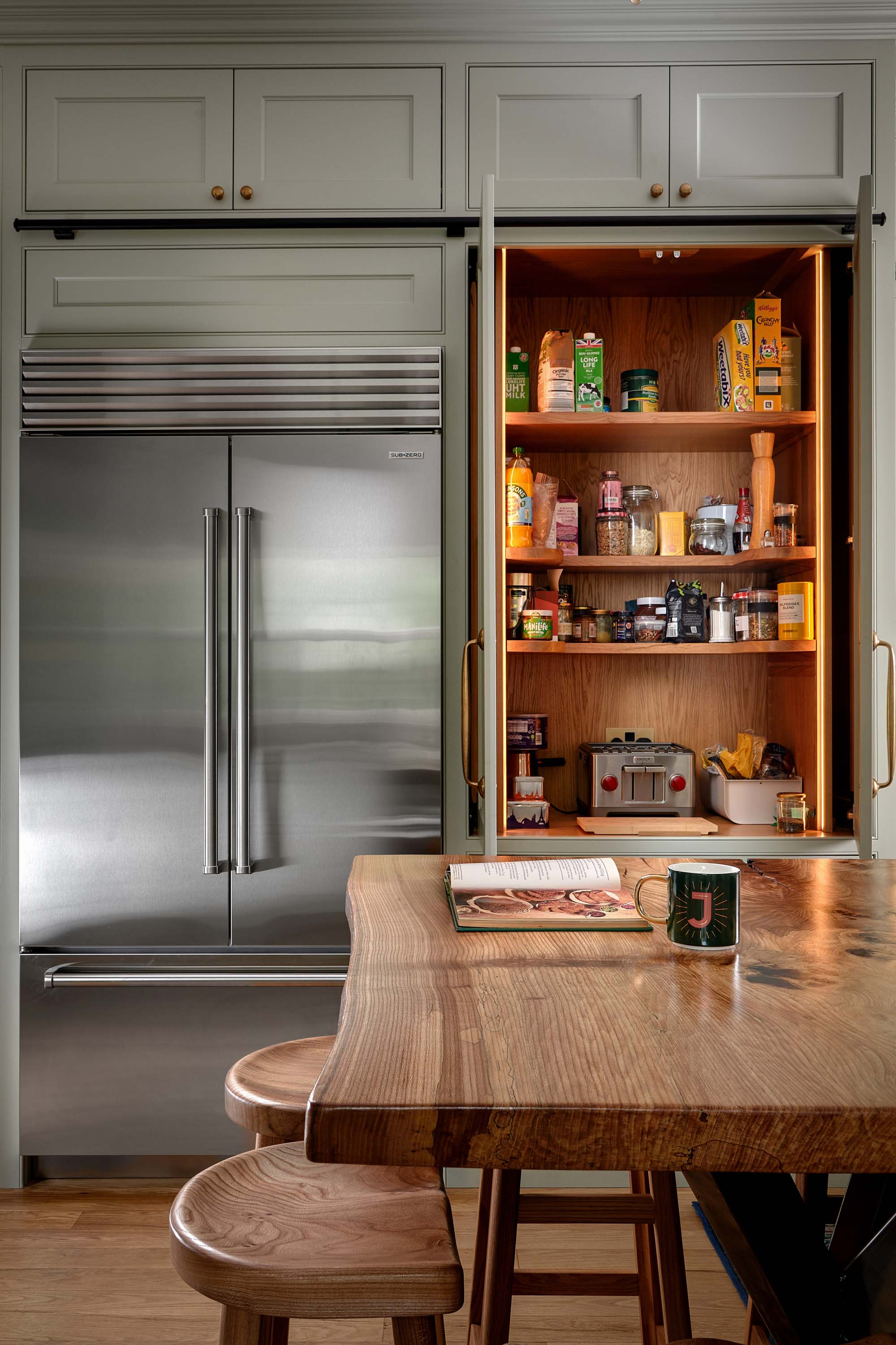 Sub zero fridge freezer and pantry cupboard with pocket doors in a traditional shaker kitchen